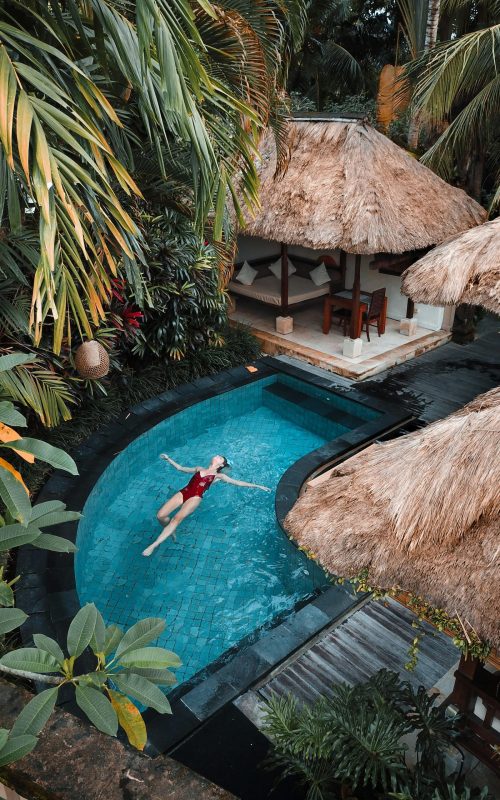 A woman enjoying leisure time floating in a tropical resort pool surrounded by lush greenery.