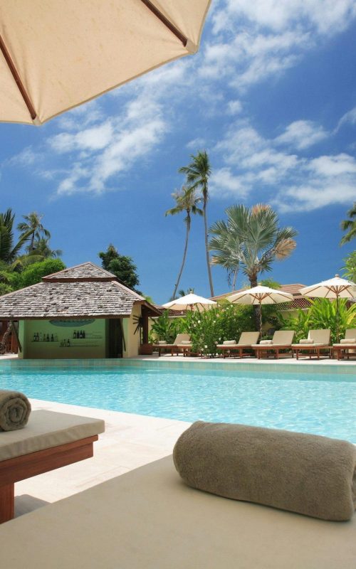 Experience ultimate relaxation at a sunlit tropical poolside resort featuring palm trees and blue skies.