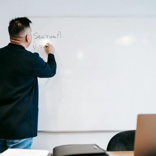 Instructor writing on a whiteboard in a classroom setting, showcasing educational engagement.