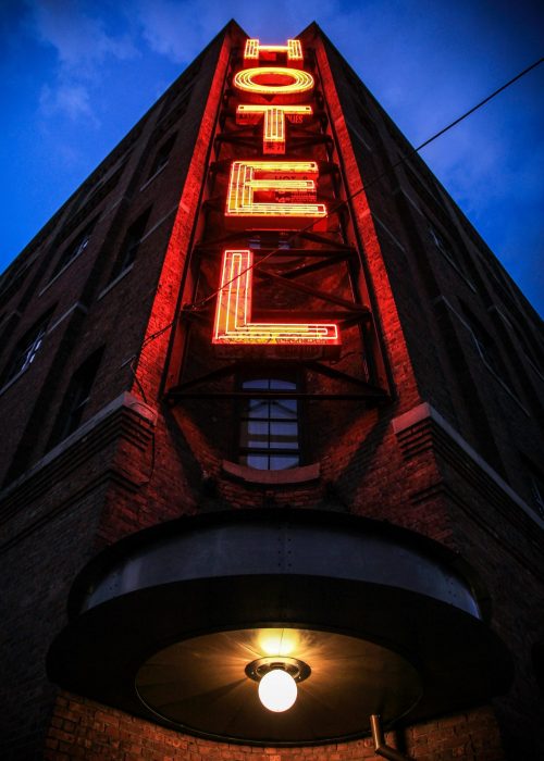 Eye-catching low angle shot of a neon hotel sign illuminating a brick building facade at dusk.